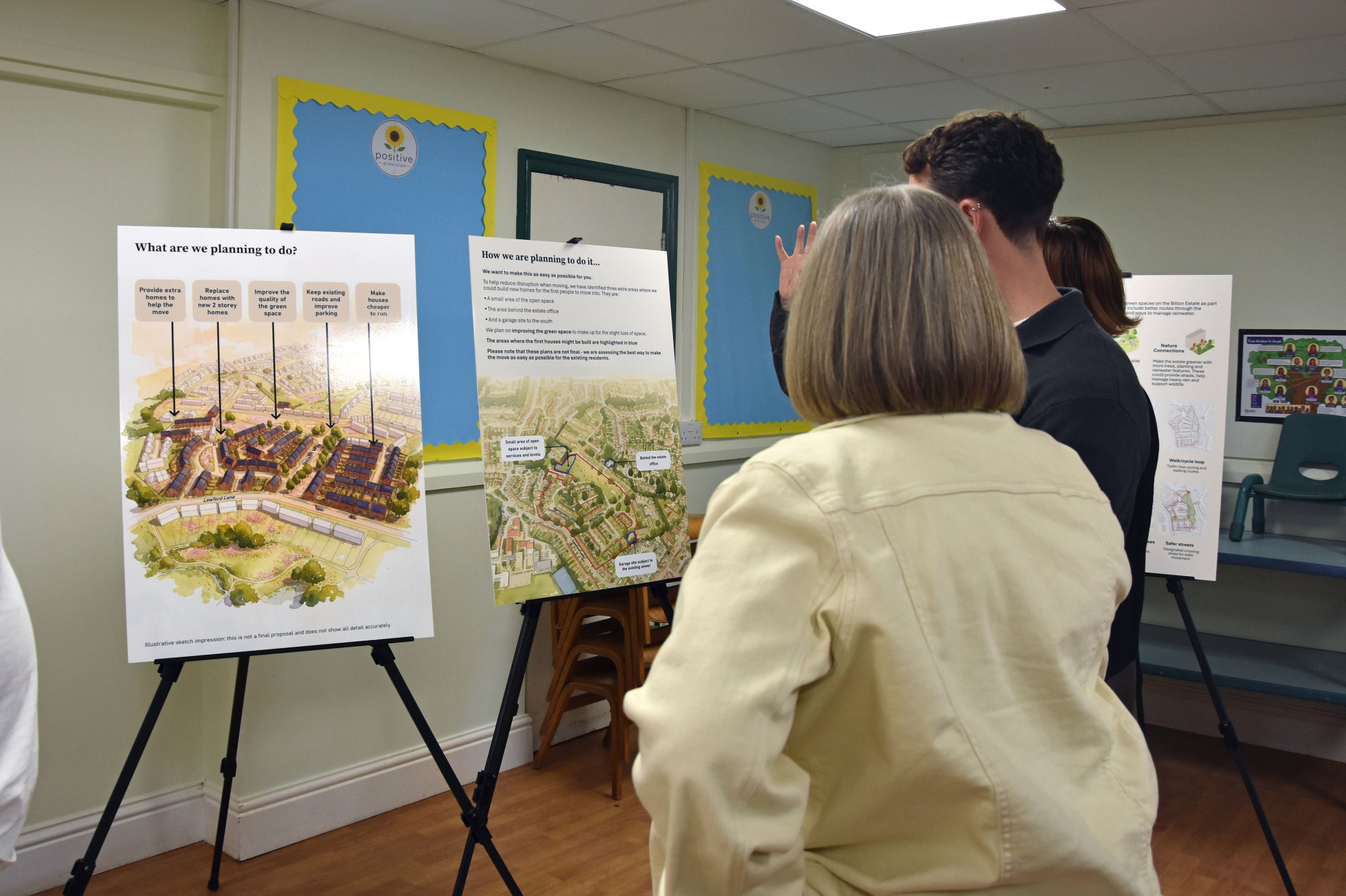 Two people looking at regeneration display boards on easels in a room, including illustrations of proposed homes and green spaces.